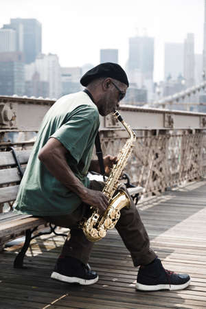Guy playing a saxophone in Brooklyn bridge. Filters added to get a dramatic look.のeditorial素材