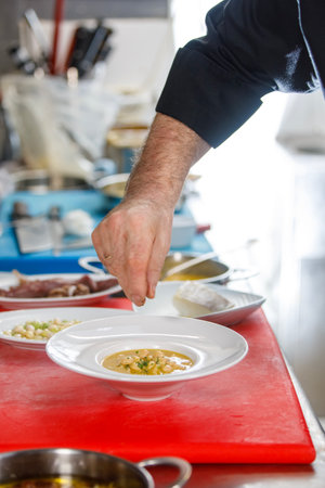 Chef is pouring some parsley over a dish of white beans in a kitchen over a cutting board.の写真素材
