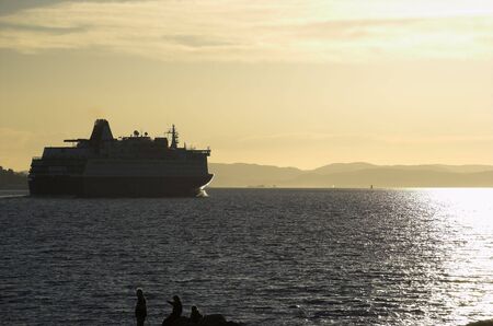 A high-contrast image of a departing ferry, sailing into the soft evening sunlight  の写真素材