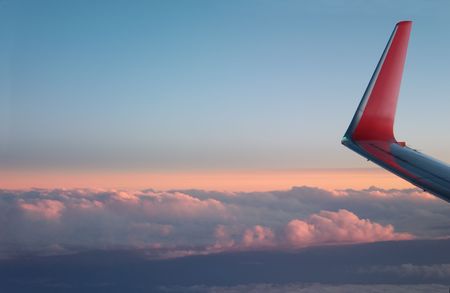 Airplane wing and clouds below, lit orange by the setting sun.  の写真素材