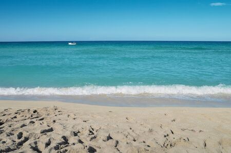 stretch of coastline of the ocean, with a white boat running along the surface of the water at the horizon,の写真素材