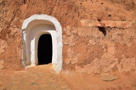 arched doorway in a mountain of red sandstone, the entrance to the traditional dwelling of cave beamsの写真素材