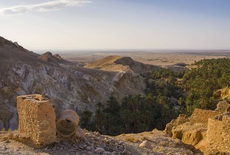 View from the height of the Atlas Mountains on the gorge, an oasis covered with palm trees, buildings and a deserted valley in the morningの写真素材