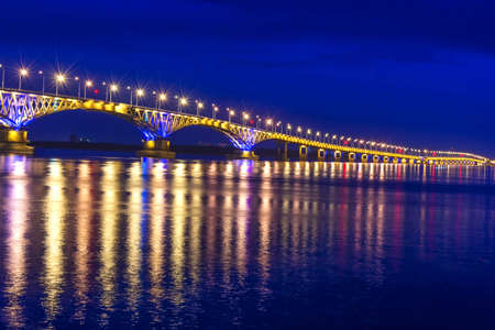 an automobile bridge across the Volga River at night, illuminated by the light of lanterns, the light of which is reflected in the river, Saratov, Russiaの写真素材