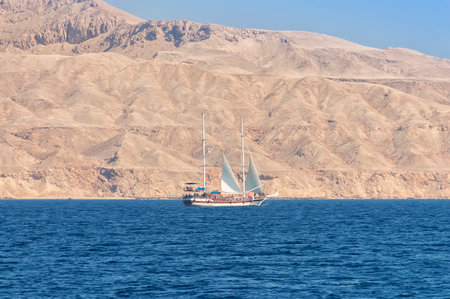 A sailboat in the sea against a background of a mountain