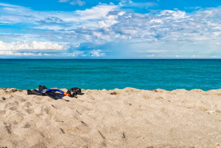 a mask for scuba diving, fins and a tube for breathing under the water on a sandy beach, against the background of the ocean and the blue sky in the clouds, Cubaの写真素材