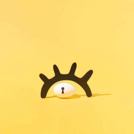 Easter egg with keyhole under black wooden eyelash against vibrant yellow background. Minimalist concept. Square layoutの写真素材