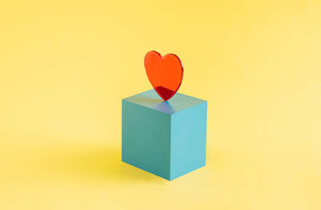 A red heart set on a blue cube isolated on a yellow background. Valentines Dayの写真素材