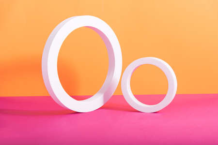 Abstract geometric composition made of two white circular frames on orange and pink background....