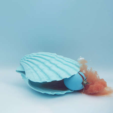 Blue sea shell and tomato with juice in the water. Summer minimal concept with healthy food. Square...