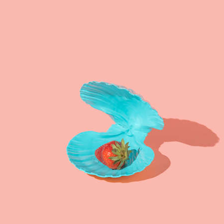 Strawberry in a blue seashell instead of pearl on a pink background. Summer minimal healthy food...