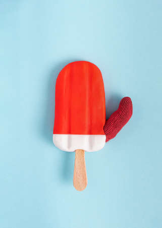 Red and white ice cream on a stick with thumb up on the blue background. Summer abstract concept. Minimal creative. Rectangle with copyspace. Phone wallpaper. Flat lay, top view.の写真素材