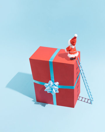 A jolly figure dressed as Santa Claus stands atop a large red gift with a blue ribbon.の写真素材