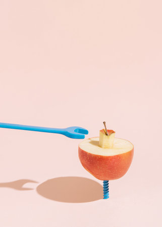 A halved apple rests on a blue screw against a pale pink background. The scene is minimalist, with the colors and simple shapes creating a striking visual contrast. Copy space on the top.の写真素材