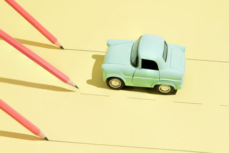 A pastel blue toy car drives down a simplistic road formed by drawn lines, while vibrant pink pencils hover above, creating an imaginative and playful scene with a modern aesthetic.の写真素材
