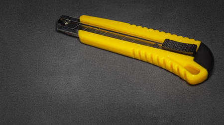 Yellow stationery office knife on dark gray surfaceの写真素材