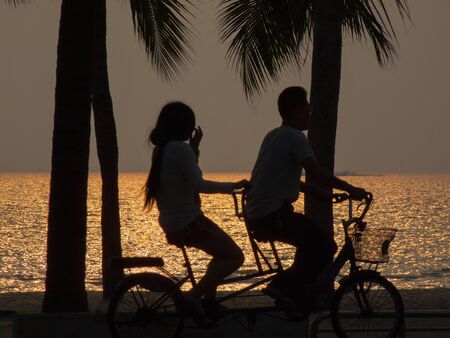 A couple riding a bicycle at sunset in Bangsaen, Thailand.の写真素材