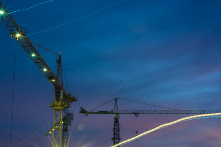 Building cranes silhouette moving against evening sky 