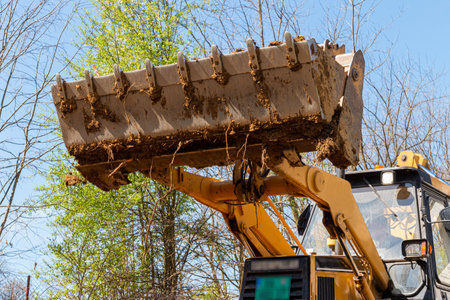 Clearing and leveling a private land plot. Yellow excavator driving earth in a wide bucketの写真素材