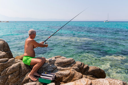 Fisherman sitting on a rock and fishing with a rodの写真素材