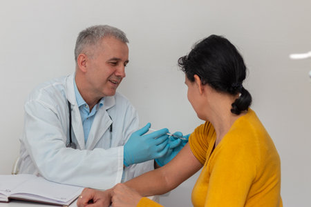 Female patient  looking at her arm while doctor in protective gloves is injecting flu vaccineの写真素材