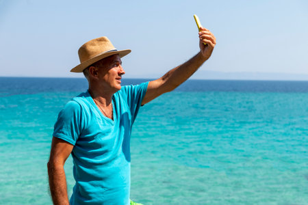 Portrait of a handsome man taking selfie. Happy mature man next to  the beach on Aegean sea. Summer vacation concept.の写真素材