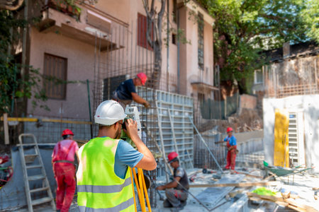 Surveying measuring equipment level theodolite on tripod at construction site with workers in backgroundの写真素材