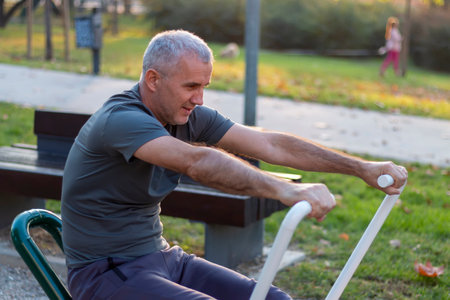 Mature man working out in the gym and leading a healthy and active lifestyle. Outdoor sports area with equipment, facilities for working out, stretching, cardio and strength physical activity.の写真素材