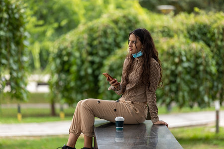 Attractive teen girl with smartphone and coffee sitting in a park and having a phone conversation. Copy spaceの写真素材
