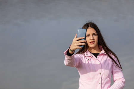 Cute young girl taking a selfie with the lake in the backgroundの写真素材