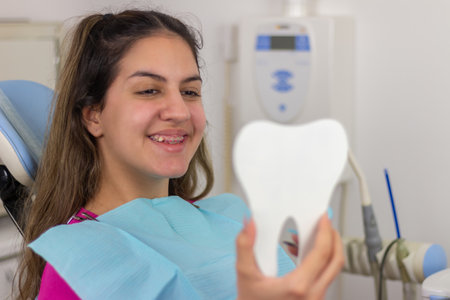 At dentist's office. Happy teen girl  looking at her braces and teeth in the mirrorの写真素材