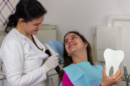Satisfied  patient. Teenager girl smiling and looking at the doctor  while sitting  at dentist's  chair after dental treatmentの写真素材