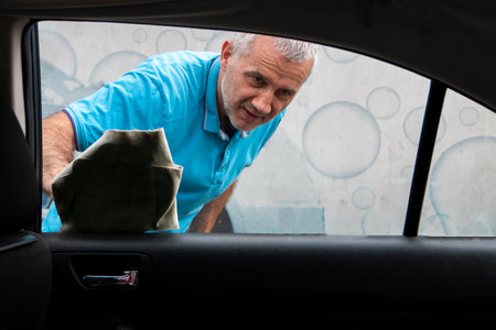 Satisfied mature man polishing his car with microfiber cloth. Close-upの写真素材