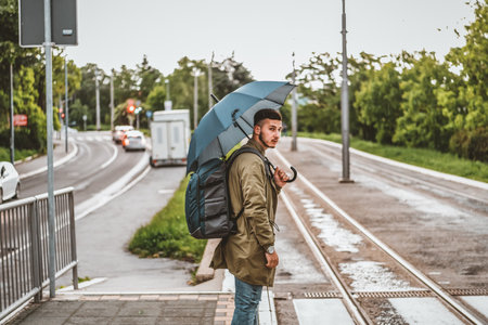 Man with umbrella crossing in the crosswalk on a rainy day. Handsome young tourist with backpack is crossing the road with umbrella.の写真素材