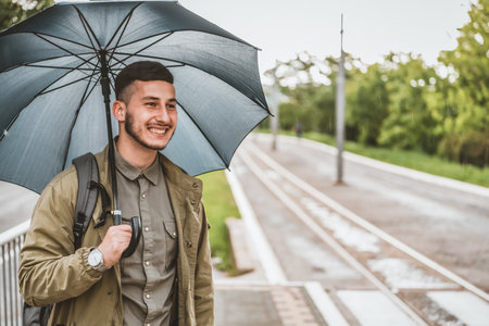 Man with umbrella crossing in the crosswalk on a rainy day. Handsome young tourist with backpack is...