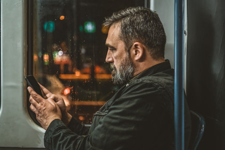 Casual man reading from mobile phone screen while traveling on metro. Wireless internet on public transport concept. Handsome hipster modern man traveling by tram in night.の写真素材
