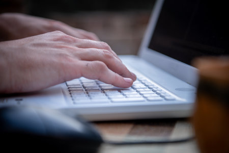 Close-up View of Male Hands Working on Laptop Outside the House. A businessman is Working on his...