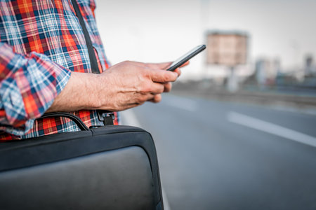 Close-up View of Businessman with Sunglasses and Plaid Shirt who is Walking in the Street and Typing Messages on his Mobile Phone. Mature Casually Dressed Man with Briefcase is Walking in the City.の写真素材