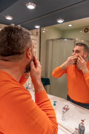 Adult man investigating his pimples on face. Guy trying to get rid of pimple squeezing it. Beauty,...