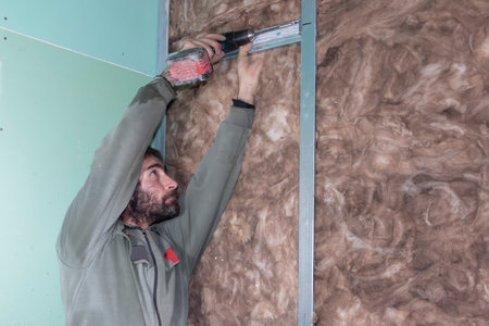 A worker installing a drywall  profile with a drill. A master fixes a profile in the bathroom. Builders apartment improvement or restoration works.の写真素材