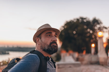 Handsome Mature Man with Beard and Hat During a Sunset in the City Near the River Bankの写真素材