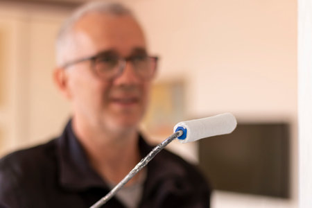 Gray-haired mature construction worker in overalls painting the wooden door with white paint. Home renovation.の写真素材