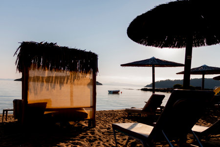Straw umbrellas and sunbeds on the beach against the background of the sea at dawn. Relaxing facilities. Holidays on the beach.の写真素材
