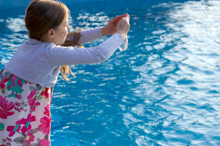 Female Teenager playing with water in front of swimming pool during summer day