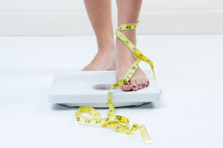 A picture of female feet standing on a bathroom scales and a tape measure 