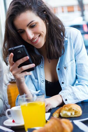 Cute young woman chatting with their smartphone at coffee shopの写真素材