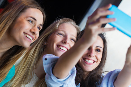 Indoor portrait of three friends taking photos with a smartphone