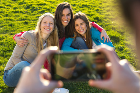 Outdoor portrait of group of friends taking photos with a smartphone in the park