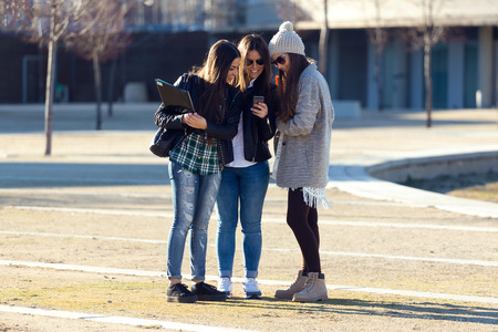 Portrait of three students girls using mobile phone in the campus.の写真素材