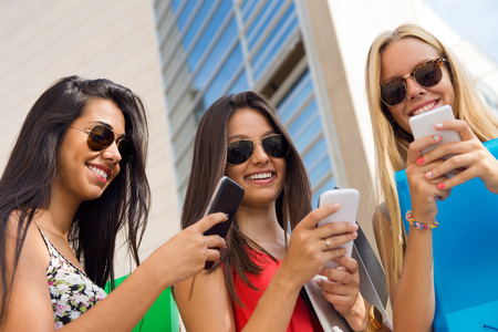 Portrait of three girls chatting with their smartphones at the campusの写真素材